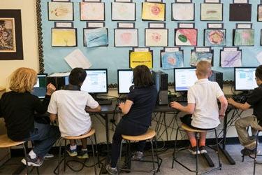 五名学生在教室里肩并肩地使用电脑