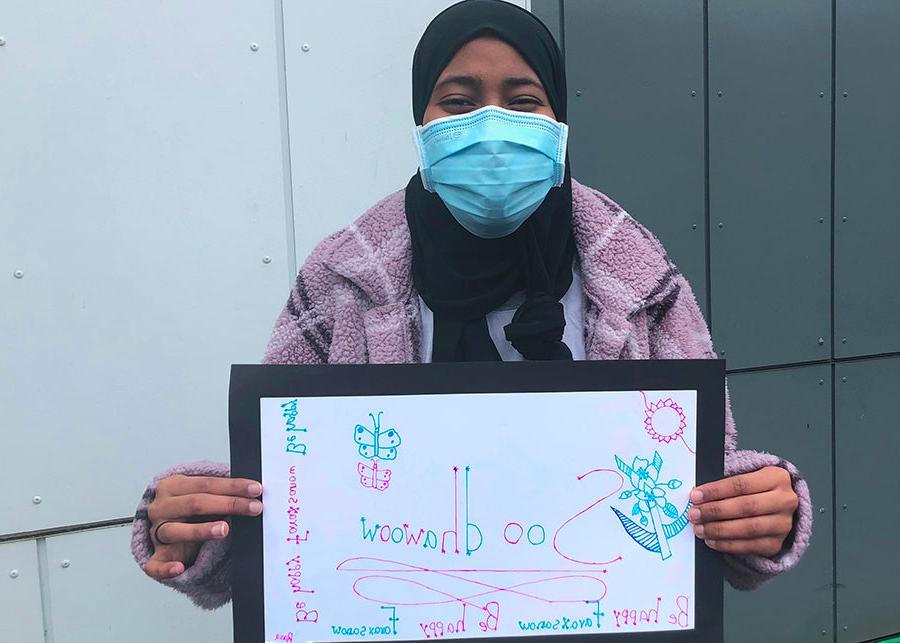 A student holds a sign that says welcome in Somali 